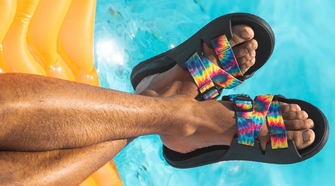 Person sporting rainbow chaco slides.