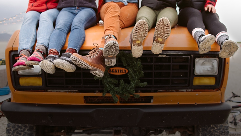 5 People sitting on the hood of a truck, wearing various Chaco sandals, shoes and boots