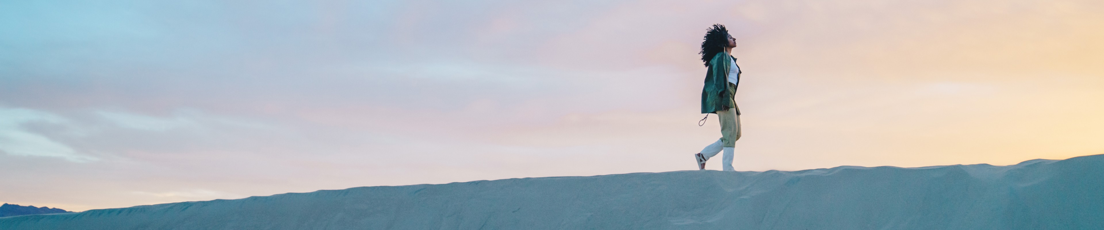 Person walking in monochrome sandals on a hill with a sunset or sunrise background.