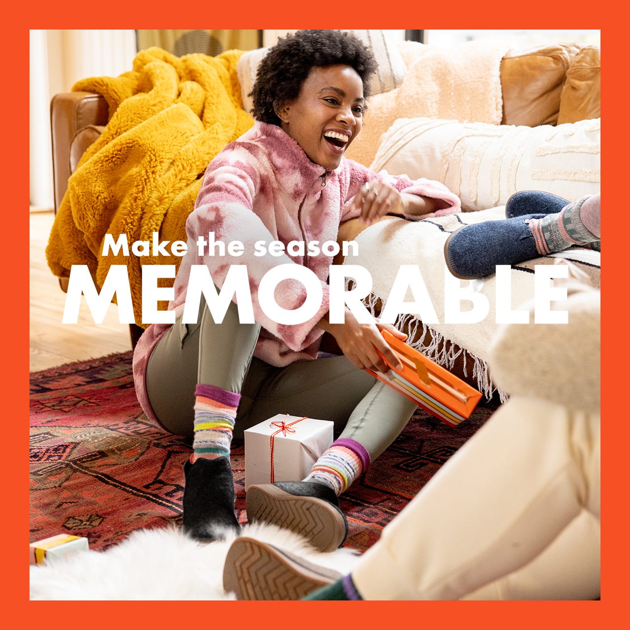 Woman opening presents by a couch with cozy Chaco moccasins.