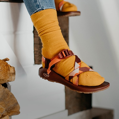 Person sitting on stairs wearing Chaco sandals and orange socks