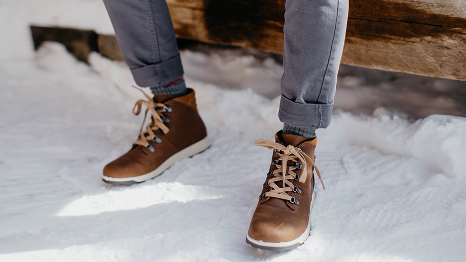 Person sitting on an outdoor bench in the snow, wearing brown Chaco boots